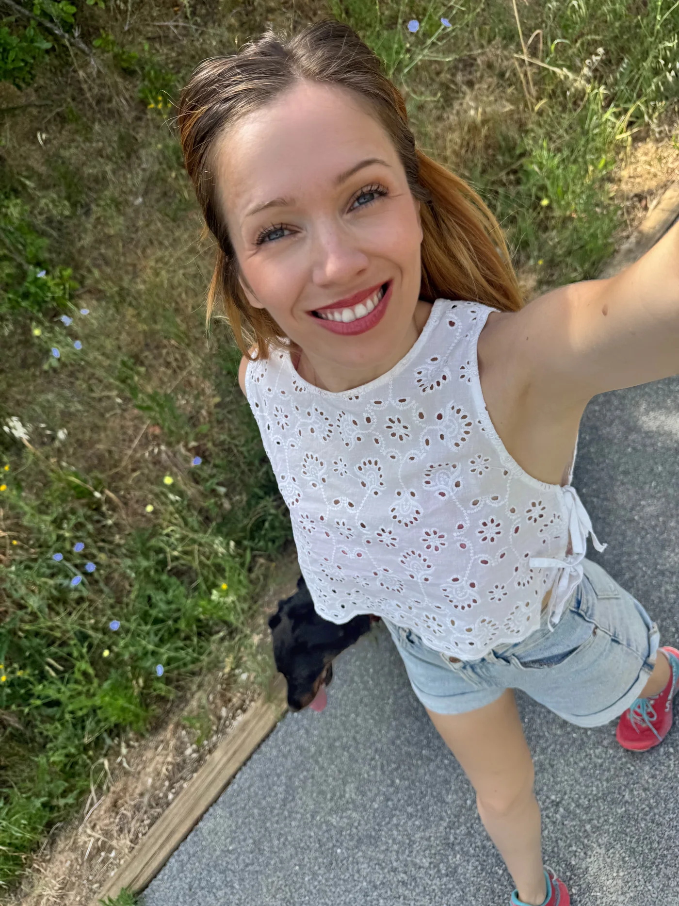 Marie-Ange en selfie sur un chemin, en haut blanc brodé, son beauceron derrière elle