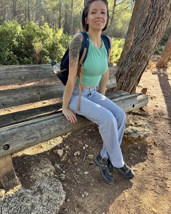 Marie-Ange en tenue de randonnée, assise sur un banc en bois dans une pinède