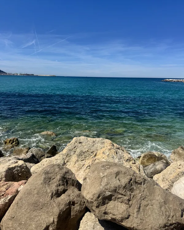 La mer turquoise et des rochers au premier plan, sous un ciel bleu