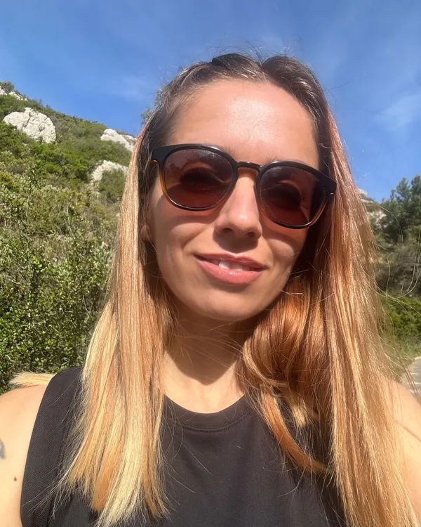 Selfie de Marie-Ange en lunettes de soleil et débardeur noir, une colline rocheuse derrière