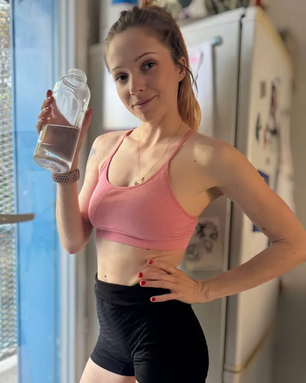 Marie-Ange en brassière rose et short noir, une bouteille d’eau à la main
